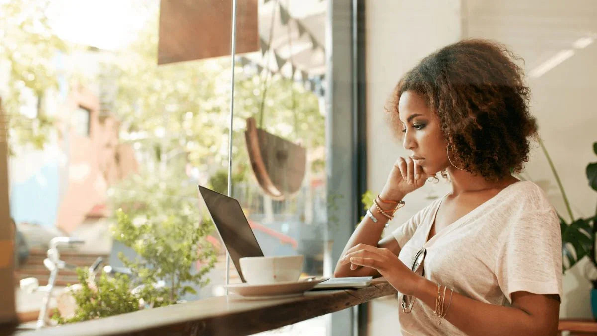 Woman using a laptop at a cafe with a view of greenery outside