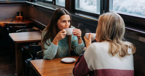 Two women sitting at a table in a restaurant, drinking coffee.