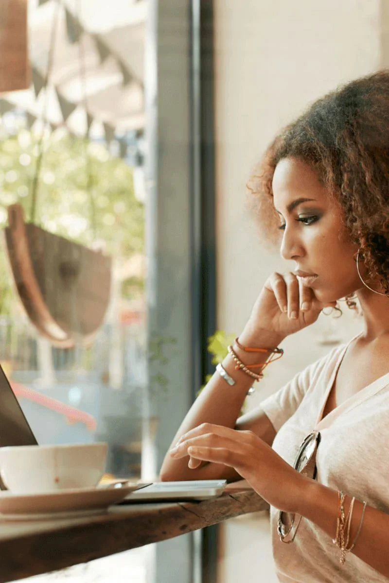 Woman sitting at a table in a cafe, looking at her phone.