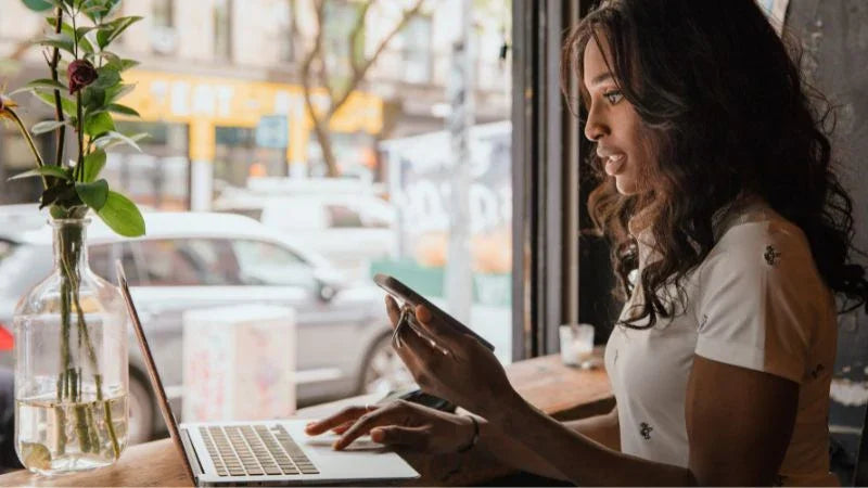 Woman using a laptop and smartphone in a cafe setting
